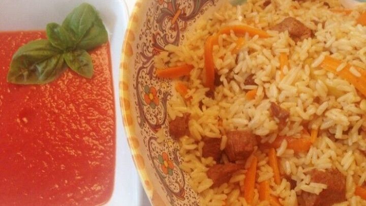Ein bunter Teller mit aromatischem Plov aus Lammfleisch und duftendem Reis, serviert mit einer roten Tomatenso&szlig;e.