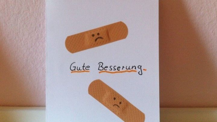 Eine Karte mit dem Text &bdquo;Gute Besserung&ldquo; und zwei Pflastern, die auf einem hellen Untergrund dekoriert ist.