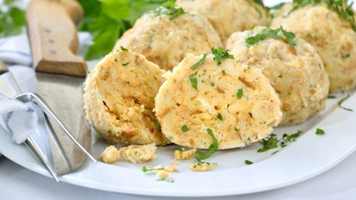 Auf einem wei&szlig;en Teller liegen frisch zubereitete Kn&ouml;del, die dekorativ mit Petersilie garniert sind, daneben ein Messer.