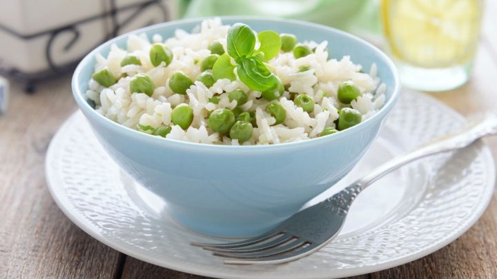 Ein blauer Sch&uuml;ssel mit mexikanischem Reis, garniert mit Erbsen und frischen Kr&auml;utern, steht auf einem rustikalen Tisch.