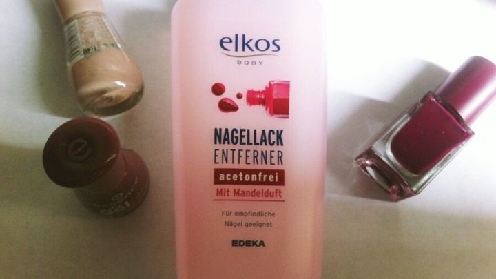 Ein Fl&auml;schchen Nagellackentferner steht auf einem Tisch, umgeben von Nagellacken in verschiedenen Farben.