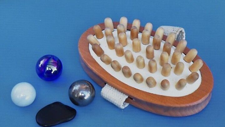 Eine Handmassageger&auml;t liegt auf einem blauen Hintergrund, umgeben von verschiedenen Massagekugeln, die zur Entspannung verwendet werden.