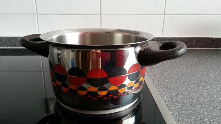 Ein bunter Kochtopf steht auf einem Herd und k&ouml;nnte durch Dampfen statt B&uuml;geln Stoffe gl&auml;tten, w&auml;hrend die Umgebung minimalistisch wirkt.