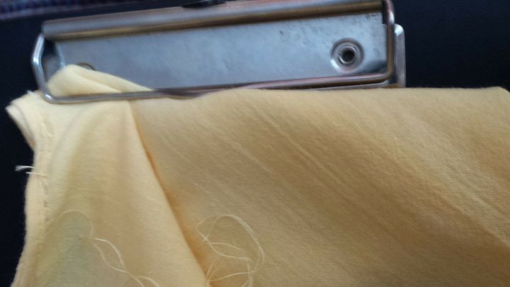 Eine Schneiderzange h&auml;lt einen gelben Stoff fest, w&auml;hrend sie am N&auml;hen in einem hellen, kreativen Bereich verwendet wird.