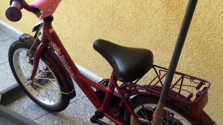 Ein rotes Kinderfahrrad steht auf einem Kiesboden, w&auml;hrend jemand versucht, es mit einem Gestell zu stabilisieren.