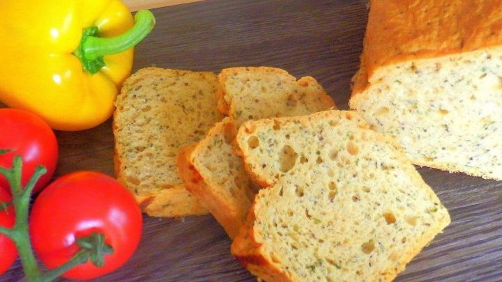 Das gesunde Brot aus rotem Linsenmehl steht auf einem Holzbrett, umgeben von frischen Tomaten und einer gelben Paprika.