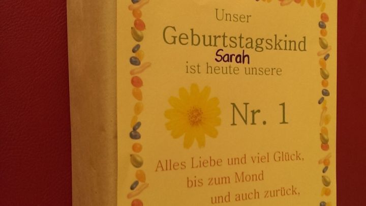Ein h&uuml;bsch verpacktes Geschenk mit einer Urkunde auf einem roten Untergrund steht im Mittelpunkt und wirkt festlich.
