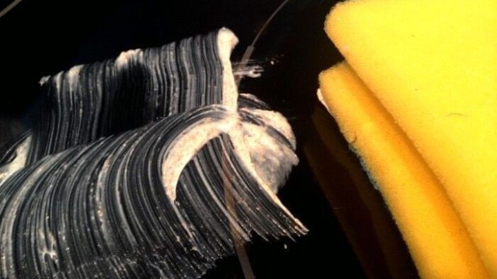 Ein glaskeramisches Feld wird mit einer Reinigungspaste bearbeitet. Im Hintergrund liegen gelbe Schw&auml;mme bereit.