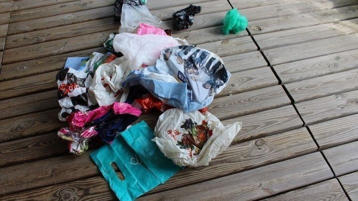 Ein Haufen bunter Plastikt&uuml;ten liegt chaotisch auf einem Holzboden, umgeben von nat&uuml;rlichem Licht im Au&szlig;enbereich.