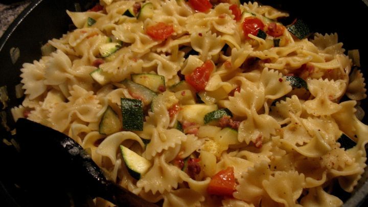 Eine bunte Mischung aus Farfalle, Gem&uuml;se und Schinkenw&uuml;rfeln wird in einer gro&szlig;en Pfanne zubereitet.