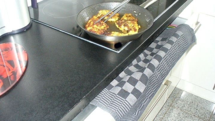 Eine Pfanne mit Braten auf einer modernen K&uuml;chenarbeitsfl&auml;che, w&auml;hrend ein Geschirrtuch bereitliegt, um Spritzer aufzufangen.