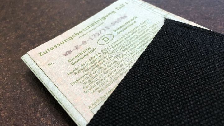 Ein verlorener Fahrzeugschein liegt auf einem Tisch, teilweise unter einem schwarzen Umschlag verborgen.