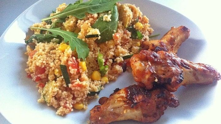 Ein bunter Couscous-Salat mit Rucola und knusprigen H&auml;hnchenst&uuml;cken auf einem wei&szlig;en Teller, appetitlich angerichtet.