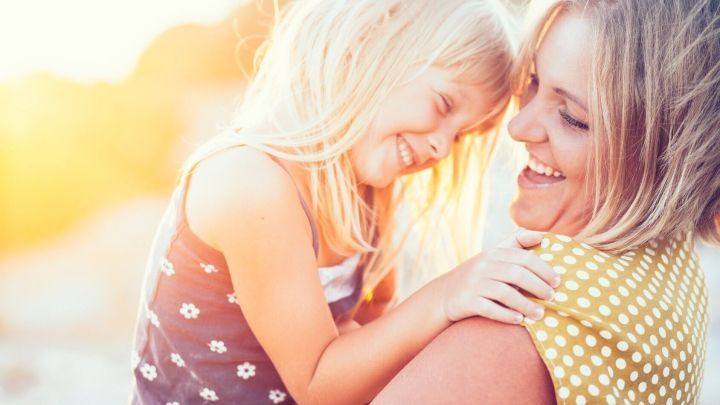 Eine l&auml;chelnde Mutter h&auml;lt ihr fr&ouml;hliches Kind in den Armen, umgeben von warmem Sonnenlicht und Harmonie.