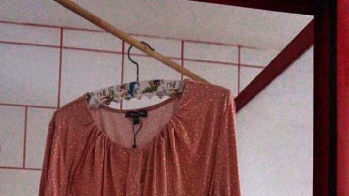 Ein nasses Hemd h&auml;ngt an einem Kleiderb&uuml;gel in der Dusche, um antrocknen zu k&ouml;nnen, umgeben von wei&szlig;en Fliesen.