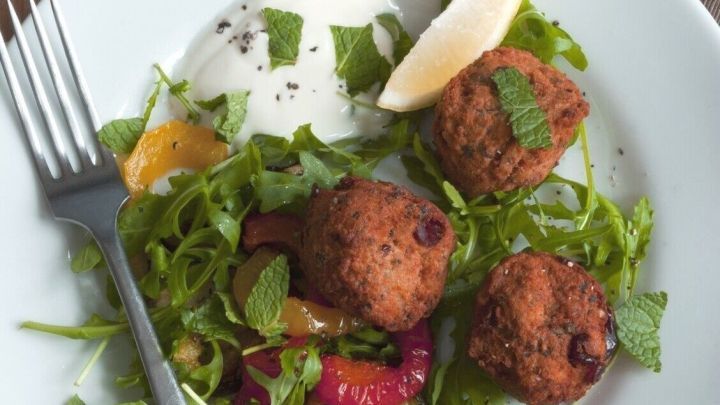 Zucchini-Falafel liegen auf einem frischen Salat, umgeben von Joghurt, und einer Zitronenscheibe. Ein perfektes vegetarisches Gericht.