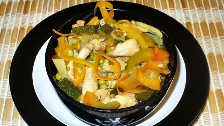 Eine kalorienarme Suppe im Asiastil, gef&uuml;llt mit buntem Gem&uuml;se, serviert in einer schwarzen Sch&uuml;ssel auf einem wei&szlig;en Teller.