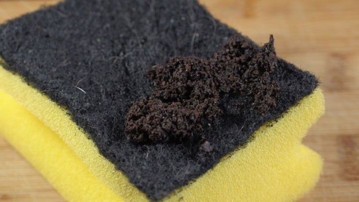 Ein Schwamm liegt auf einer Holzoberfl&auml;che, bedeckt mit Kaffeesatz, bereit zum Gebrauch zur Reinigung des Grillrosts.
