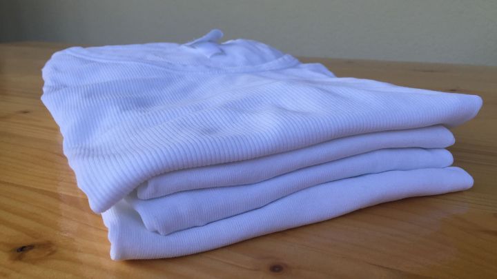 Sauber gefaltete alte Baumwollunterhemden liegen ordentlich auf einem Holztisch, bereit f&uuml;r die Wiederverwendung oder weitere Nutzung.