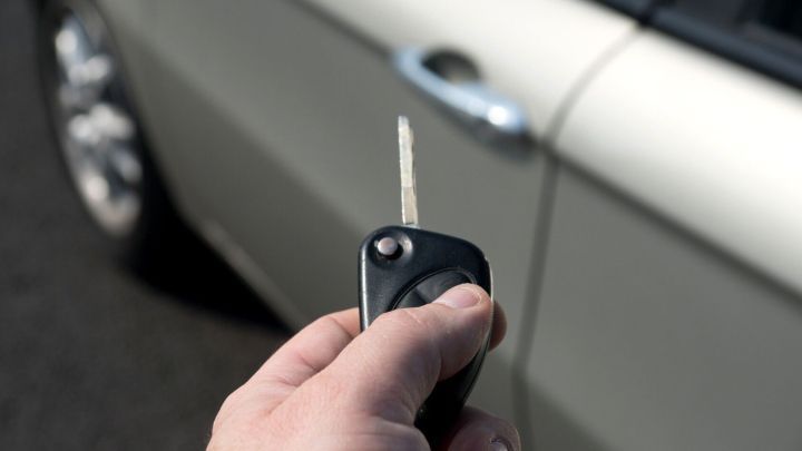 Ein Autoschl&uuml;ssel wird in der Hand gehalten, w&auml;hrend er darauf abzielt, ein Auto zu entriegeln, das in der N&auml;he steht.