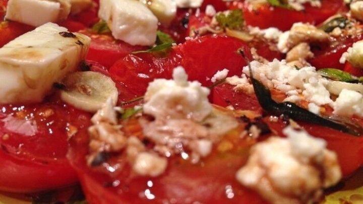 Saftige Ofentomaten liegen auf einem Teller, belegt mit Knoblauch und K&auml;se, umgeben von frischen Kr&auml;utern.