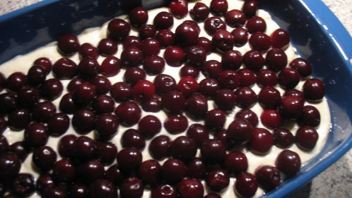 Ein Kirsch-Quark-Auflauf liegt in einer blauen Auflaufform, gef&uuml;llt mit einer Schicht Quark und bedeckt von vielen Kirschen.