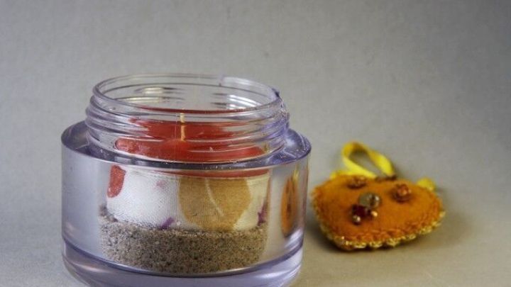 Eine leere Cremedose enth&auml;lt ein Teelicht und liegt auf einer flachen Oberfl&auml;che neben einer Dekoration aus getrockneten Bl&uuml;ten.