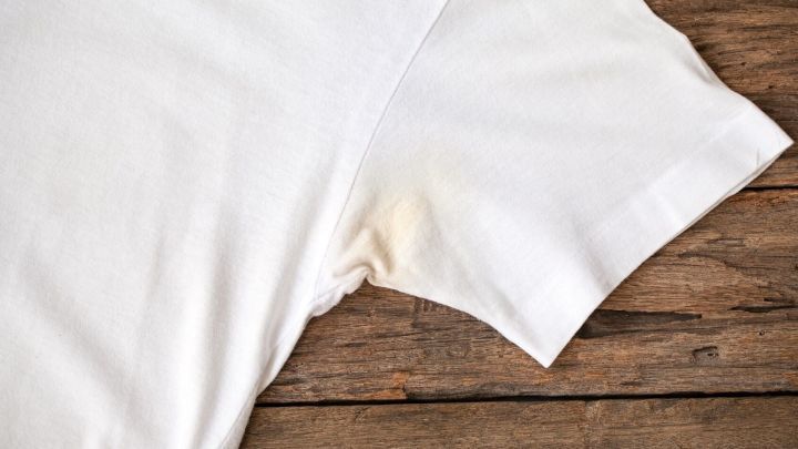 Ein wei&szlig;es T-Shirt mit Deoflecken liegt auf einem Holztisch, bereit zur Reinigung oder Fleckentfernung.