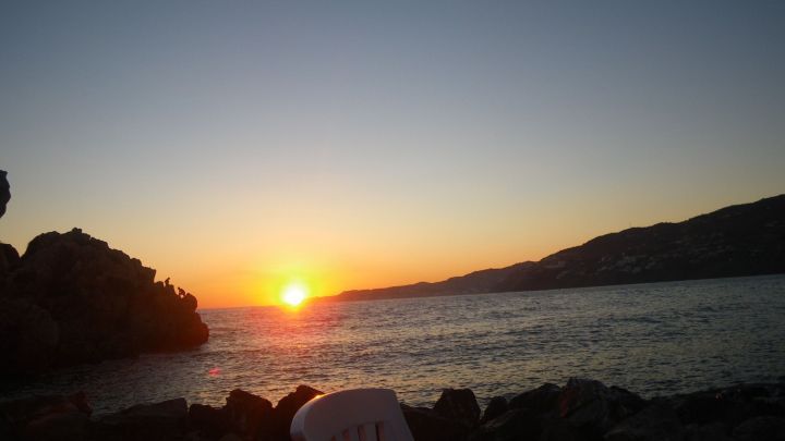 Sonnenuntergang &uuml;ber dem Meer, w&auml;hrend der Hund am Ufer spielt. Entspanntes Ambiente an der K&uuml;ste Spaniens mit Blick auf die Felsen.