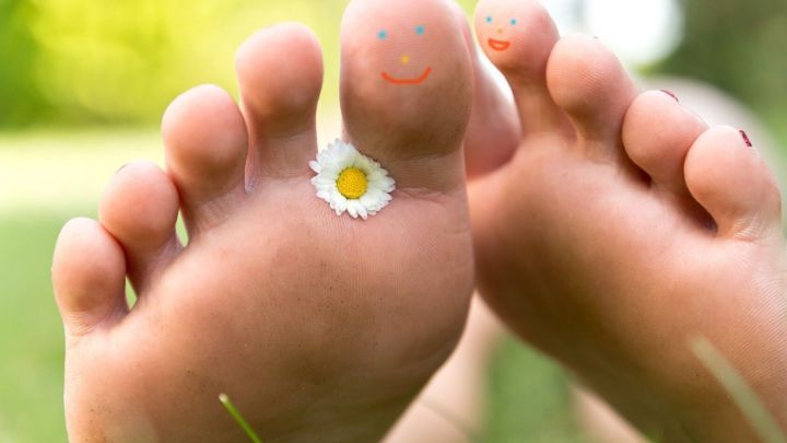 Barfu&szlig;f&uuml;&szlig;e mit einer bl&uuml;henden Blume liegen auf gr&uuml;nem Gras und strahlen Freude und Gesundheit aus, ideal gegen Fu&szlig;pilz.