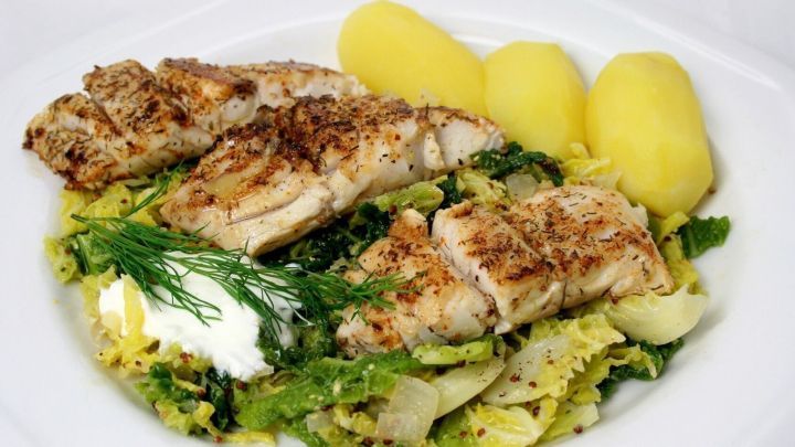 Fischfilet liegt auf einem Bett aus gr&uuml;nem Gem&uuml;se, dazu Kartoffeln, alles liebevoll angerichtet auf einem wei&szlig;en Teller.