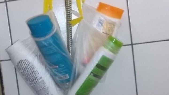 Mehrere Duschgel-Flaschen h&auml;ngen an einem Duschschlauch in einer gefliesten Dusche, die mit einem gelben Band gesichert sind.