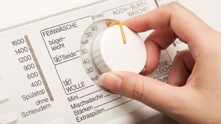 Eine Hand dreht den Waschmaschinenregler, um die W&auml;sche richtig zu waschen. Die Maschine steht in einem Wohnraum.