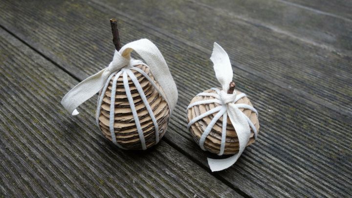 Zwei dekorative Objekte aus Pappe liegen auf einer Holzoberfl&auml;che und sind mit B&auml;ndern geschm&uuml;ckt, ideal f&uuml;r Tischdekoration.