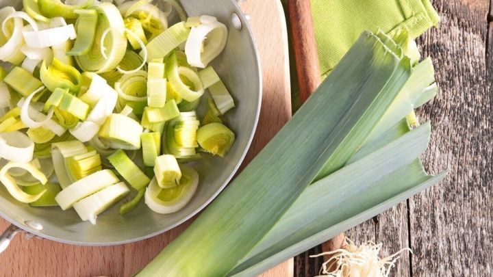Geschnittenes asiatisches Porreegem&uuml;se liegt in einer Sch&uuml;ssel zusammen mit einem Holzl&ouml;ffel auf einem Holzbrett.