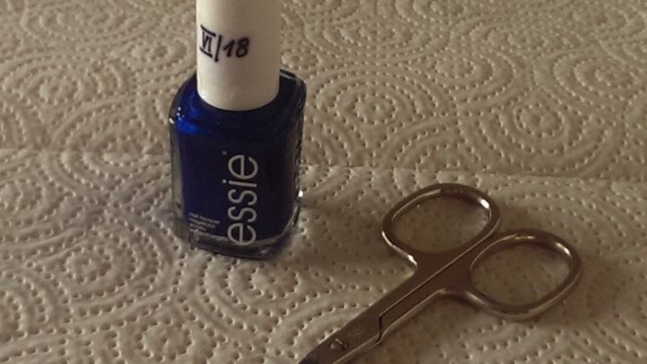 Ein blauer Nagellack steht neben einer kleinen Schere auf einer K&uuml;chenarbeitsfl&auml;che mit Pappetuch.