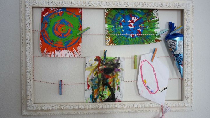 Ein leerer Bilderrahmen dient als kleine Kunstgalerie, in der bunte Kinderzeichnungen auf einer Schnur h&auml;ngen.