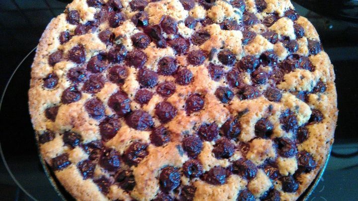 Ein runder Sauerkirschkuchen mit einer goldbraunen, kr&uuml;meligen Oberfl&auml;che steht auf einer dunklen Oberfl&auml;che.