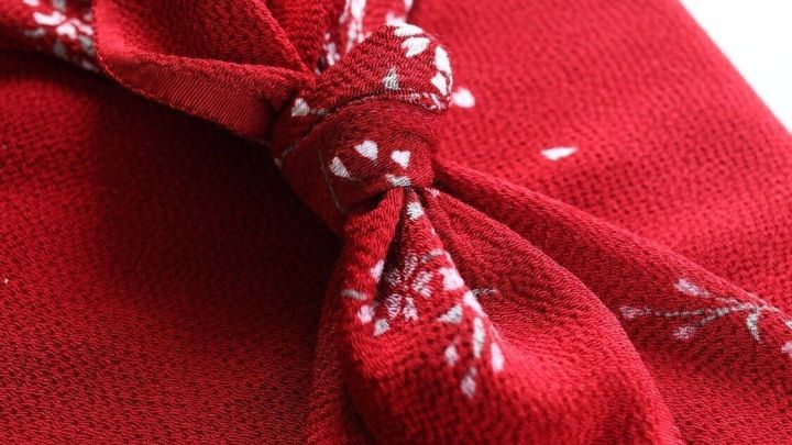 Ein rot verpacktes Geschenk zeigt eine Furoshiki-Technik, die umweltfreundlich statt Plastik verwendet wird.