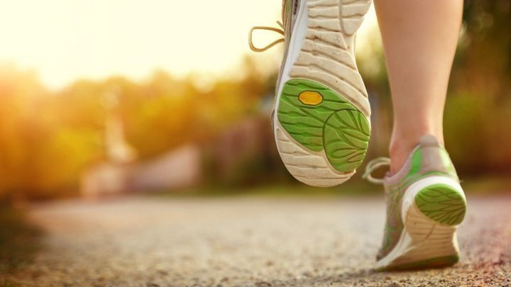 Laufschuhe mit gr&uuml;nem Profil laufen auf einem sonnigen Weg, umgeben von bl&uuml;hender Natur und sanftem Licht.
