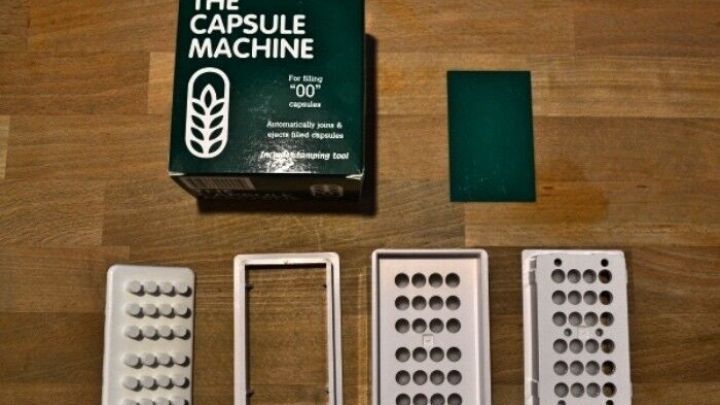 Eine Kapselmaschine steht auf einer Holzoberfl&auml;che, umgeben von Kapselh&auml;lften zur Bef&uuml;llung mit Inhalt.