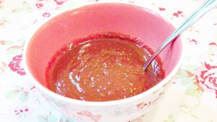 Eine Sch&uuml;ssel mit pikante Grillso&szlig;e steht auf einem blumigen Tisch, w&auml;hrend ein L&ouml;ffel die So&szlig;e umr&uuml;hrt.