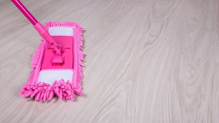 Ein pinker Wischmopp reinigt einen Laminatboden in einem hellen Raum, der Geradlinigkeit und Sauberkeit vermittelt.