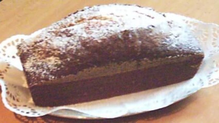 Ein rechteckiger Kuchen mit Puderzucker bedeckt steht auf einer Spitzendecke auf einem Holztisch.