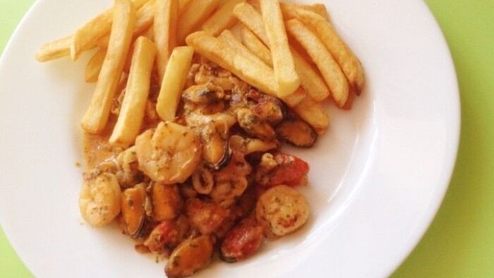 Ein Teller Meeresfr&uuml;chte-Cocktail liegt neben knusprigen Pommes frites auf einer hellgr&uuml;nen Oberfl&auml;che.