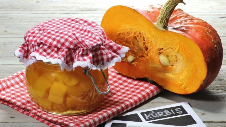 Ein Glas eingekochtes Gem&uuml;se steht auf einem Tisch neben einem aufgeschnittenen K&uuml;rbis, alles ist rustikal dekoriert.