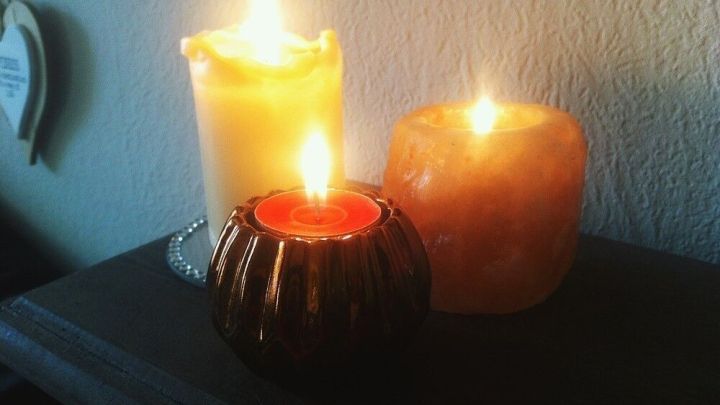 Drei brennende Kerzen stehen auf einem Regal. Die Flammen erzeugen warmes Licht, das eine gem&uuml;tliche Atmosph&auml;re schafft.