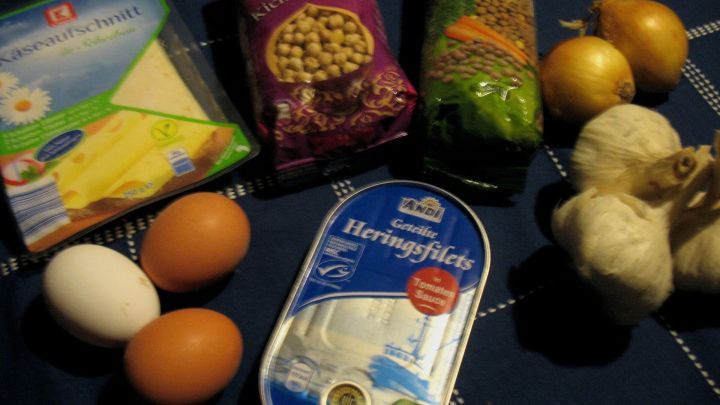 Eier liegen auf einem blauen Tuch, umgeben von verschiedenen Lebensmitteln wie Knoblauch, Zwiebeln und einer Frischk&auml;severpackung.