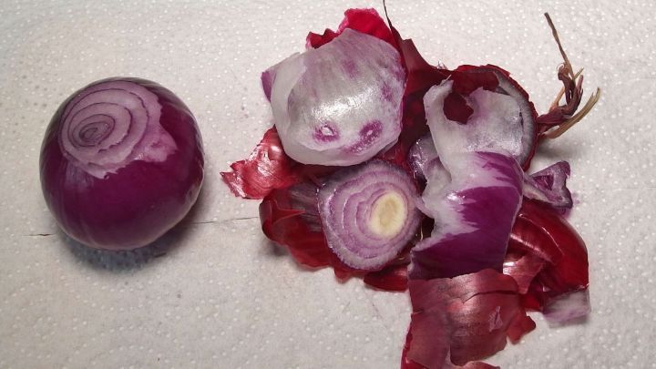 Eine Zwiebel liegt neben ihren abgezogenen Schalen auf einer wei&szlig;en Oberfl&auml;che, die den Reinigungsprozess zeigt.