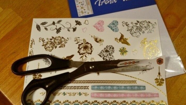 Auf einem Tisch liegen Scheren und Bl&auml;tter mit trendigen, tempor&auml;ren Tattoos, bereit zur Anwendung ohne Reue.